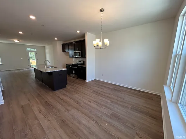 an empty room with wooden floor and kitchen view