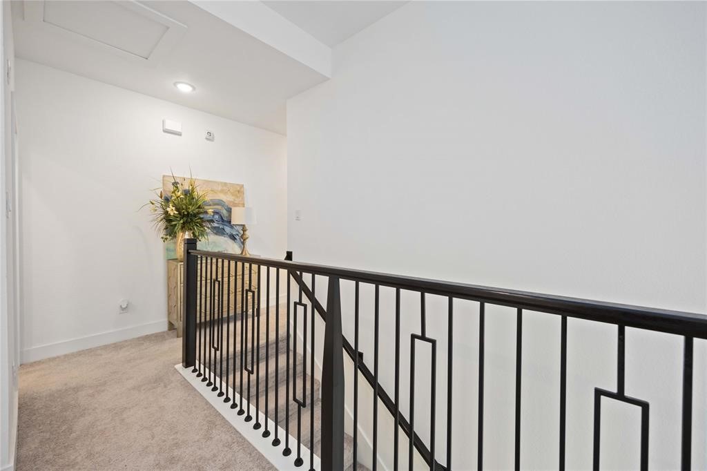 10014 Nectar Path Iowa Colony, TX 77583 - Photo 13 of 26 This photo shows a bright hallway with plush carpeting, a modern black metal railing, and a decorative plant on a console table against a white wall.