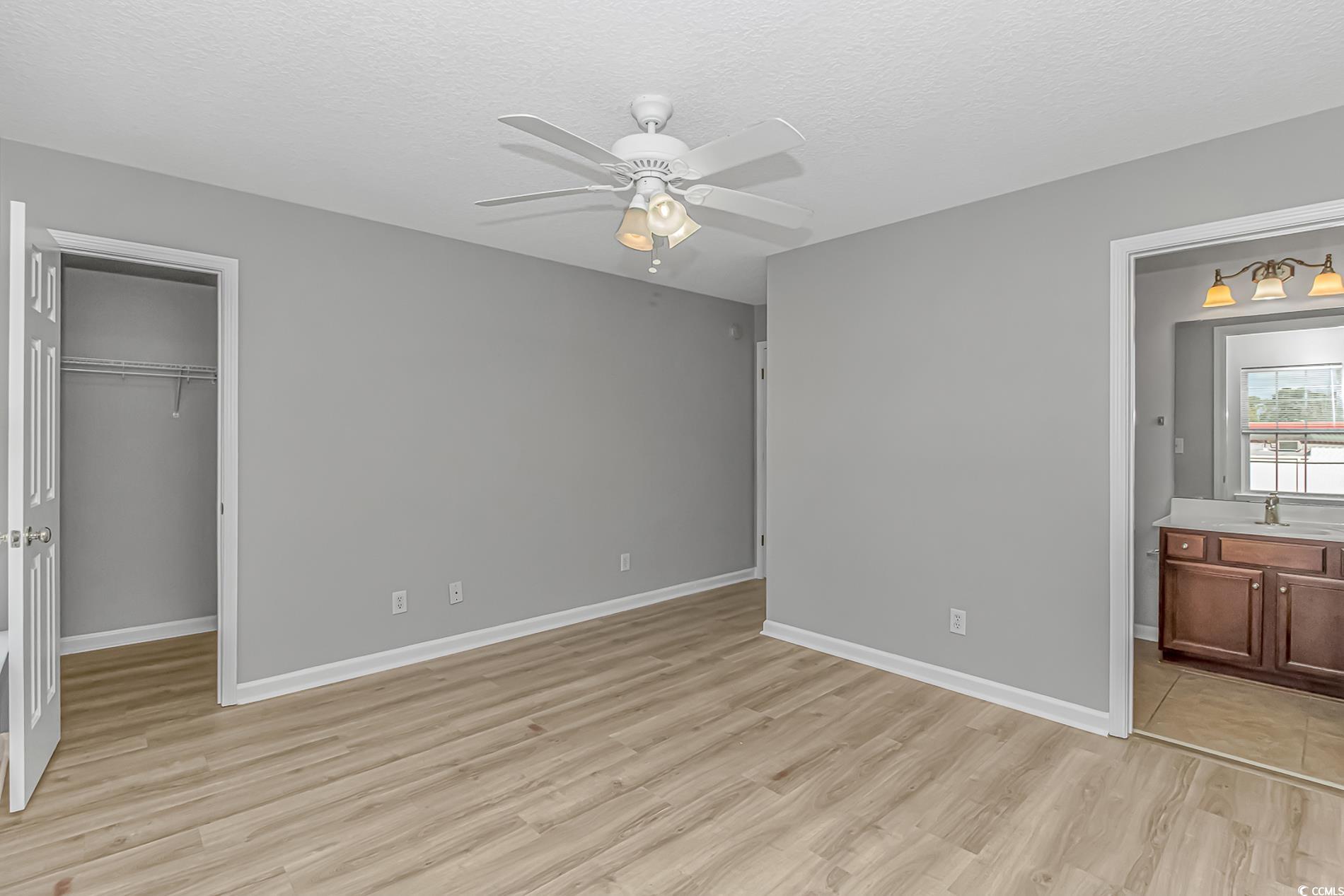 502 Lake Shore Drive Surfside Beach, SC 29575 - Photo 19 of 25 Unfurnished bedroom featuring a textured ceiling, light wood-style flooring, a spacious closet, ceiling fan, and connected bathroom