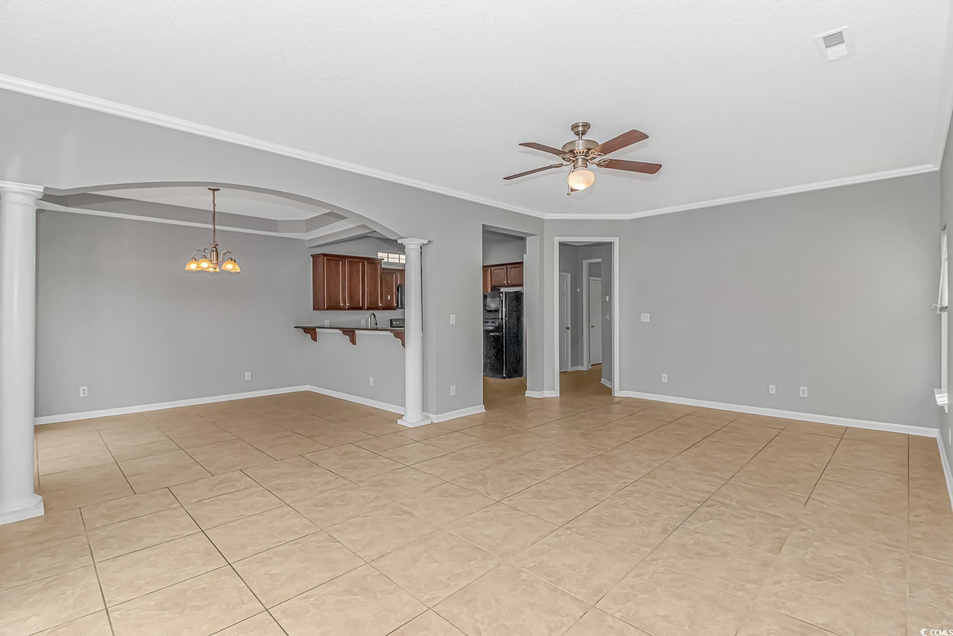 502 Lake Shore Drive Surfside Beach, SC 29575 - Photo 6 of 25 Unfurnished living room featuring a chandelier, decorative columns, crown molding, light tile patterned floors, and a ceiling fan