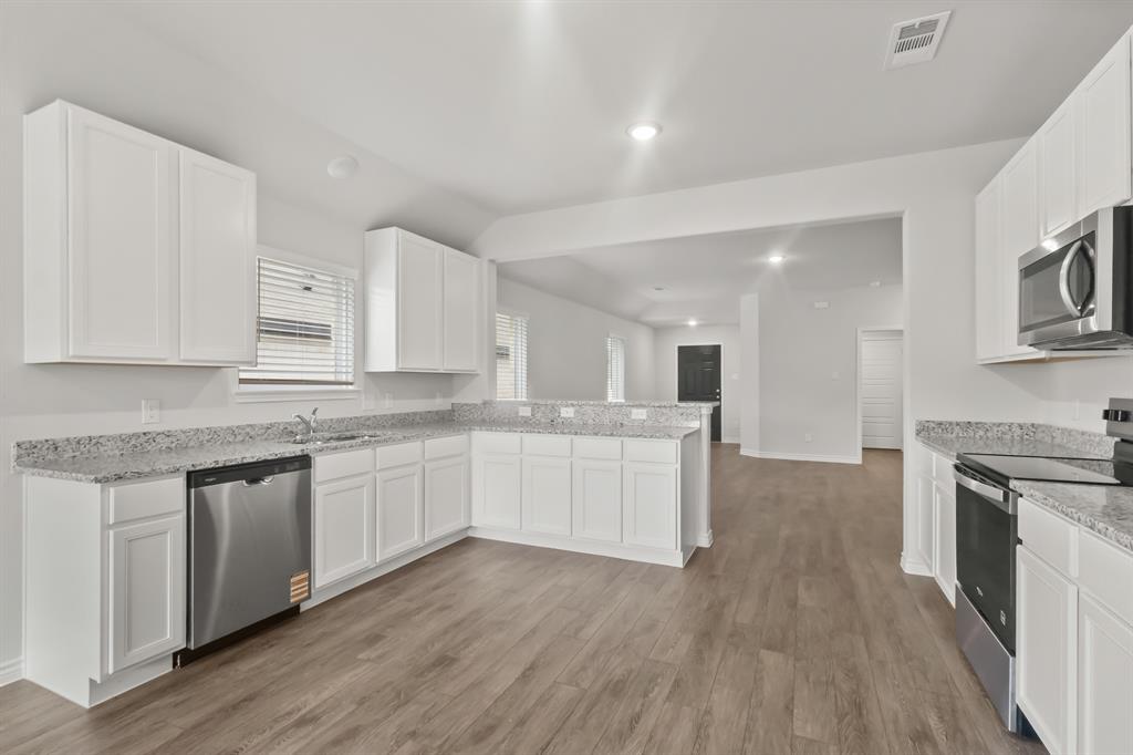 1607 Romans Road Ennis, TX 75119 - Photo 5 of 15 a large kitchen with granite countertop a stove top oven a sink dishwasher and a white cabinets with wooden floor