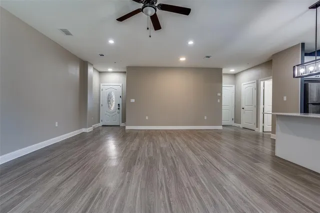 a view of an empty room with wooden floor and a ceiling fan