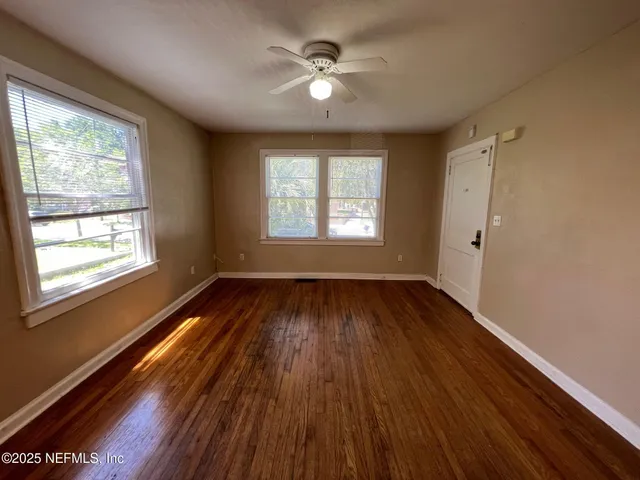 a view of an empty room with wooden floor and a window