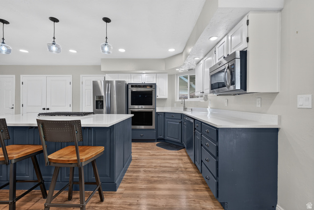 1690 Maplewood Way St. George, UT 84790 - Photo 5 of 17 Chef's kitchen featuring custom cabinetry in white and navy finishes, stainless steel appliances including double wall ovens, quartz countertops, waterfall island with seating for two, and pendant lighting