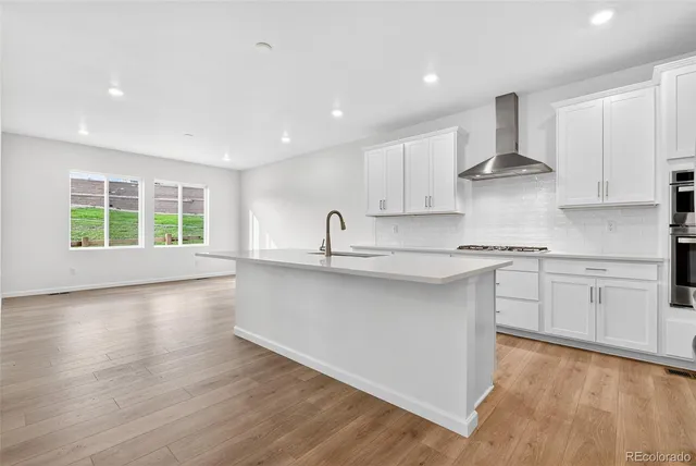 a kitchen with stainless steel appliances granite countertop a stove a sink and white cabinets with wooden floor