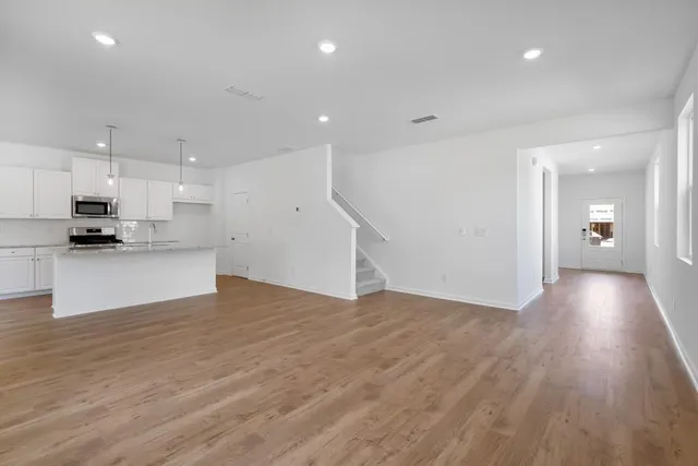 a view of an empty room and kitchen with wooden floor