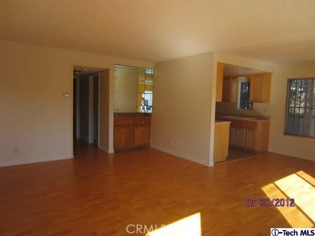 an empty room with kitchen view and wooden floor