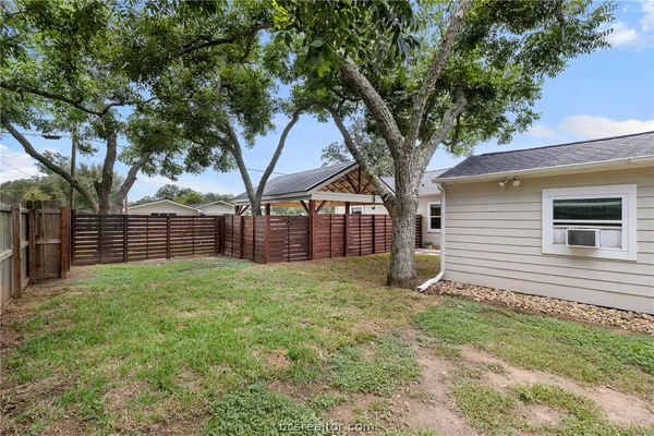 a view of a backyard with large trees and wooden fence