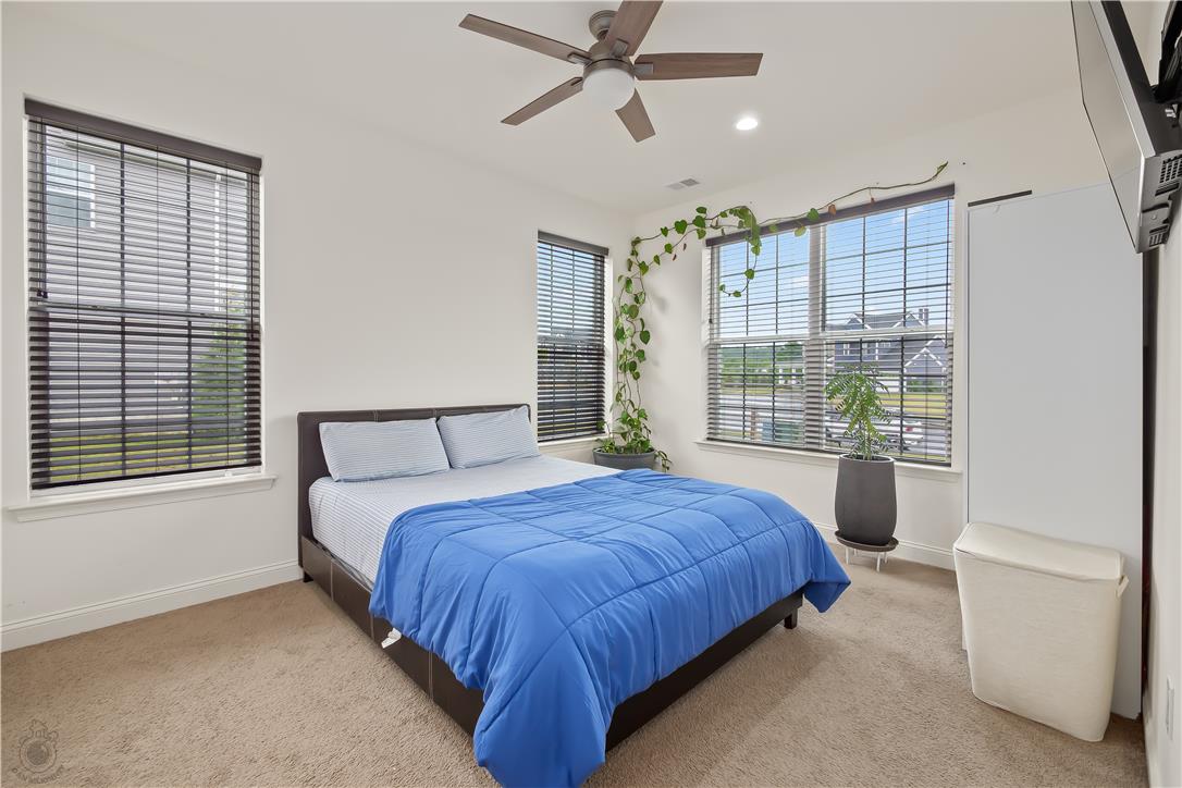 A well-lit bedroom features plush carpeting, a wide window with blinds, and a contemporary ceiling fan for comfort.