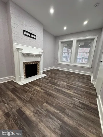 a view of an empty room with wooden floor fireplace and a window