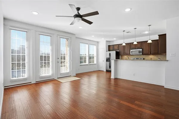 a view of an empty room with wooden floor and a kitchen