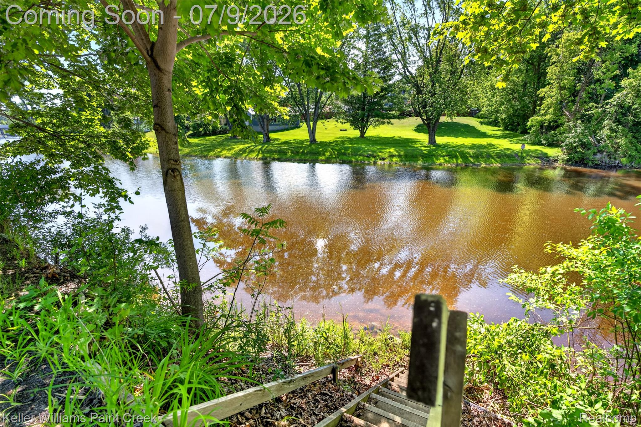 204 Russell Road Kawkawlin, MI 48631 - Photo 19 of 82 Waterside property featuring a wooden staircase descending to the water's edge, mature trees providing natural shade, and lush green landscaping