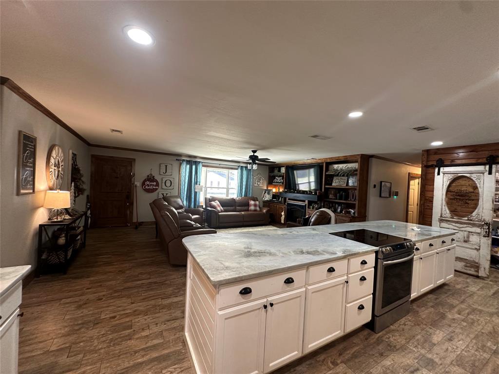 101 Twin Creek Road Comanche, TX 76442 - Photo 15 of 28 Kitchen featuring stainless steel electric range, a barn door, light stone counters, a ceiling fan, and a fireplace