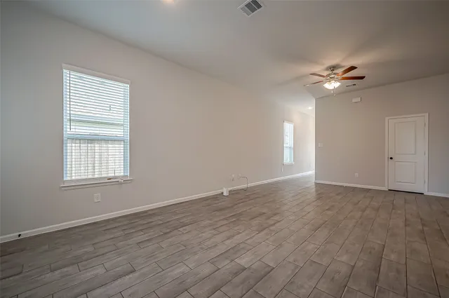 an empty room with wooden floor ceiling fan and windows
