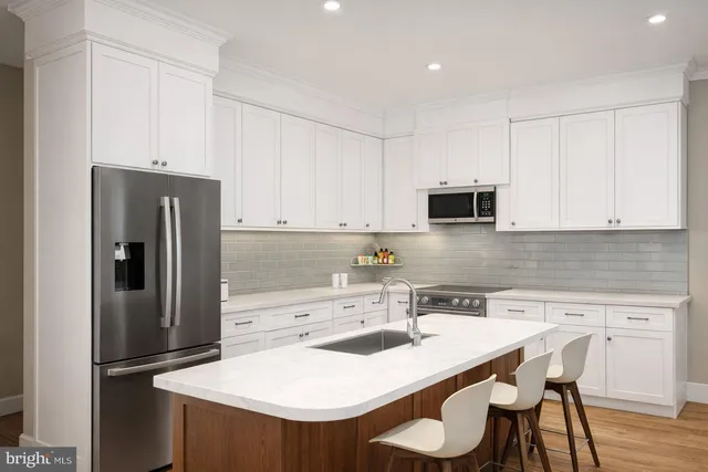 a kitchen with stainless steel appliances a sink a microwave a refrigerator and white cabinets