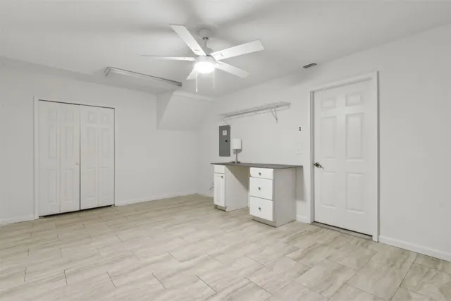 an empty room with chandelier fan and kitchen view