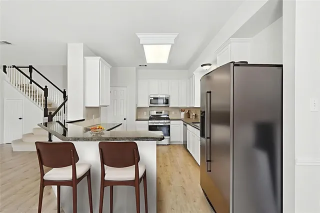 a kitchen with stainless steel appliances granite countertop a refrigerator a sink a stove and chairs