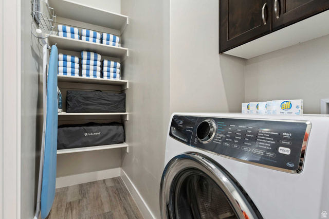 2600 Ocotillo Way, Unit 31 Santa Clara, UT 84765 - Photo 35 of 73 Dedicated laundry area featuring a front-loading washing machine, built-in shelving, dark wood-finish upper cabinetry, light gray wall paint, and wood-finish flooring