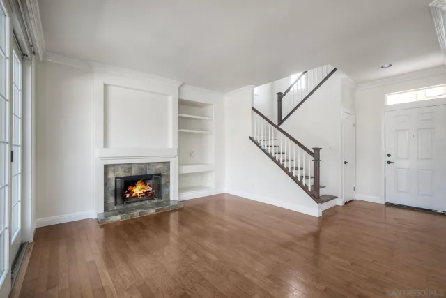 a view of an empty room with wooden floor fireplace and a window