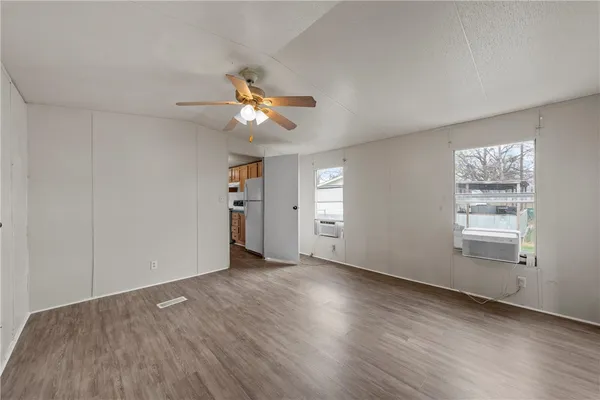 an empty room with wooden floor chandelier fan and windows