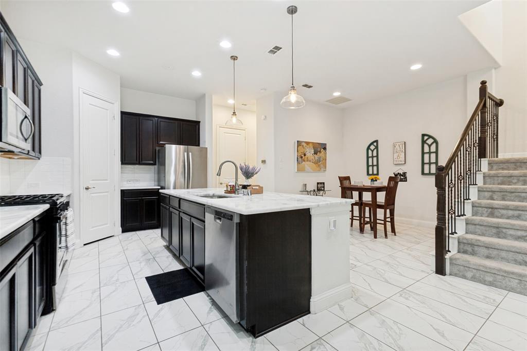 605 Ansley Way Allen, TX 75013 - Photo 9 of 28 Modern kitchen featuring dark cabinetry, stainless steel appliances, a center island with sink, and white tile flooring