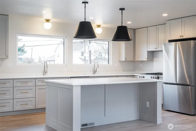 a kitchen with stainless steel appliances granite countertop a sink a stove a refrigerator and island with wooden floor