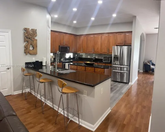 a kitchen with stainless steel appliances kitchen island granite countertop a refrigerator a sink and wooden cabinets