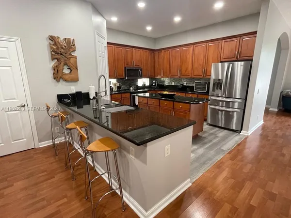 a kitchen with granite countertop stainless steel appliances a sink a stove a refrigerator cabinets and wooden floor