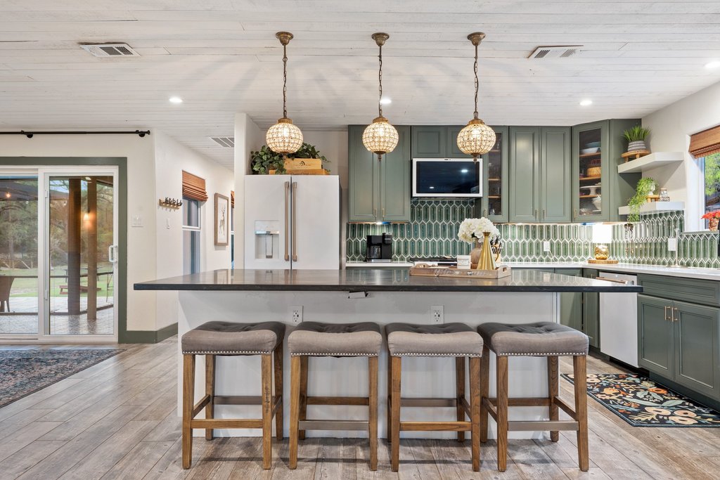 2800 River Road Wimberley, TX 78676 - Photo 11 of 40 Kitchen featuring a kitchen breakfast bar, backsplash, pendant lighting, glass insert cabinets, and two tone color scheme