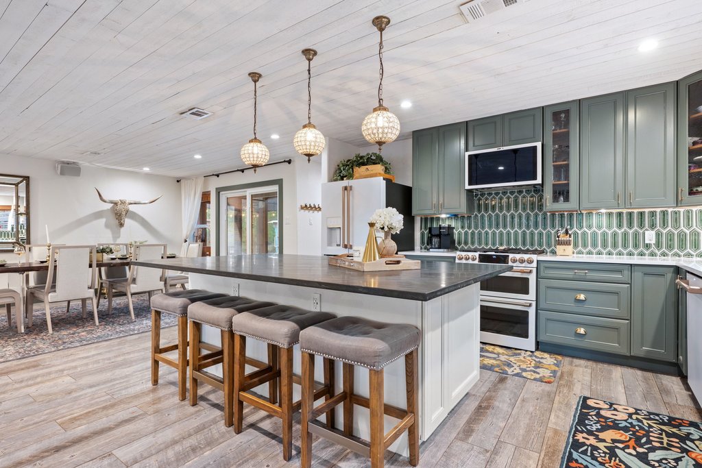 2800 River Road Wimberley, TX 78676 - Photo 12 of 40 Two tone kitchen featuring a breakfast bar area, two tone cabinets, glass insert cabinets, decorative light fixtures, and high end appliances