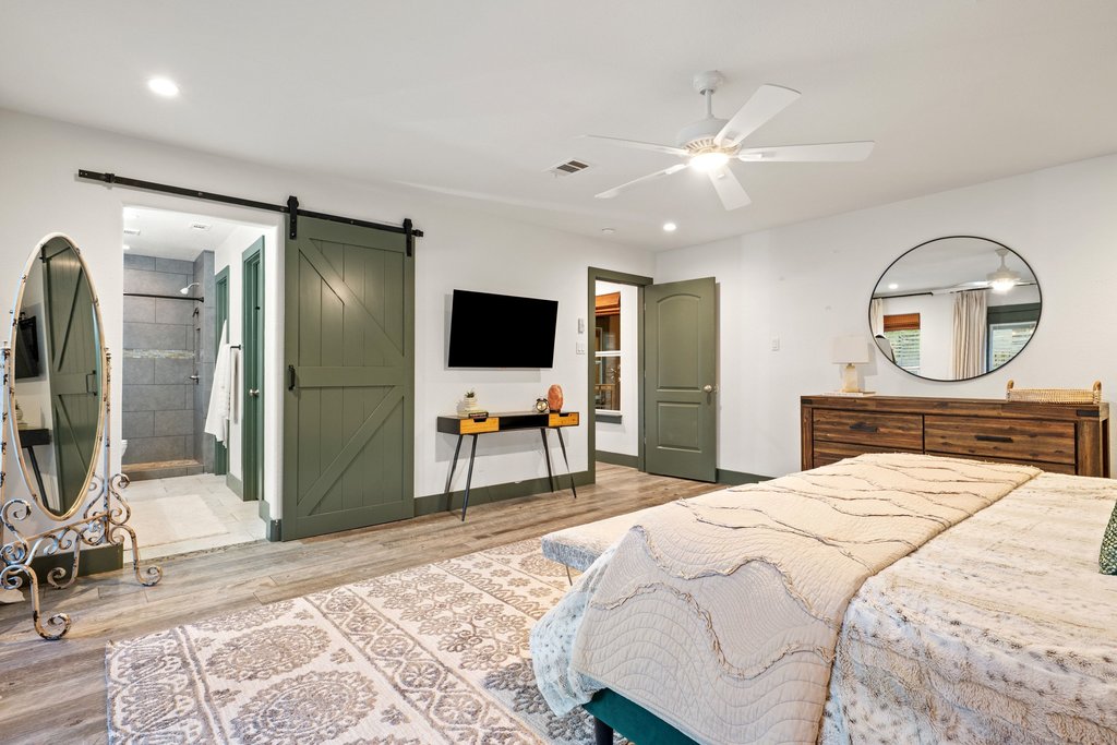 2800 River Road Wimberley, TX 78676 - Photo 19 of 38 Bedroom featuring a barn door, light wood-style floors, a ceiling fan, ensuite bath, and recessed lighting