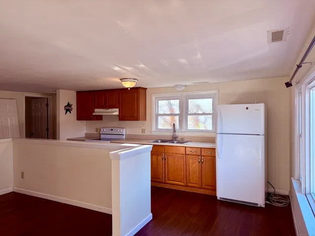 a kitchen with stainless steel appliances granite countertop a refrigerator a sink dishwasher a stove top oven a dining table and chairs with wooden floor