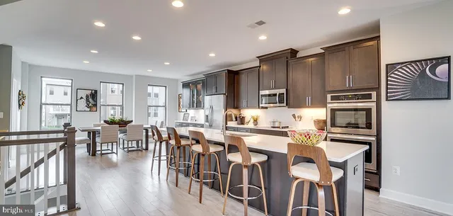 a kitchen with stainless steel appliances granite countertop a stove top oven a refrigerator a dining table and chairs with wooden floor