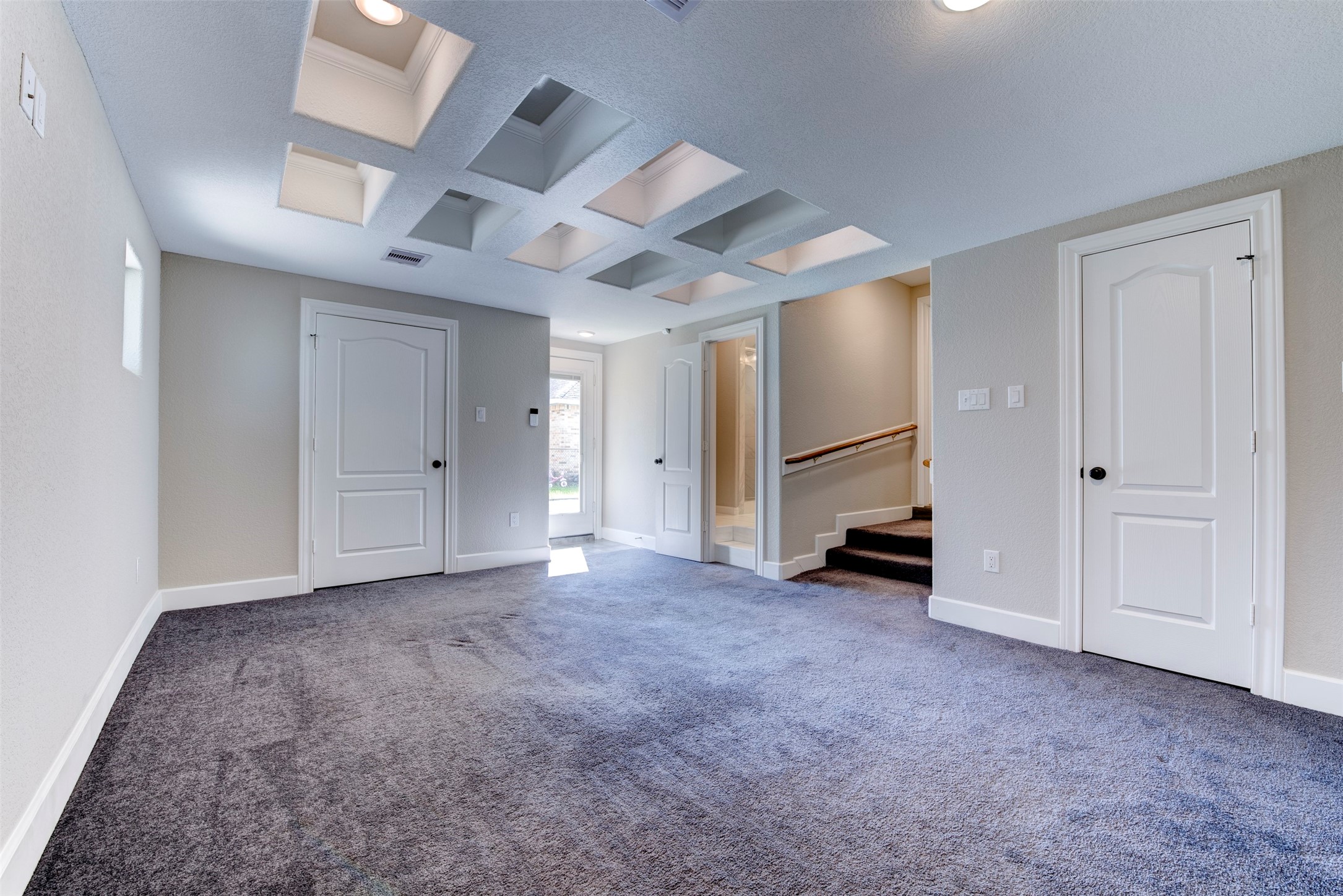 109 Dresden Street Houston, TX 77012 - Photo 25 of 43 Recessed lighting, and a unique coffered ceiling design. It has multiple doors leading to the patio, a stairway with a handrail, and natural light from small windows, creating a bright and inviting atmosphere.