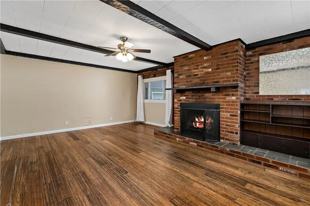 a view of an empty room with wooden floor fireplace and a window