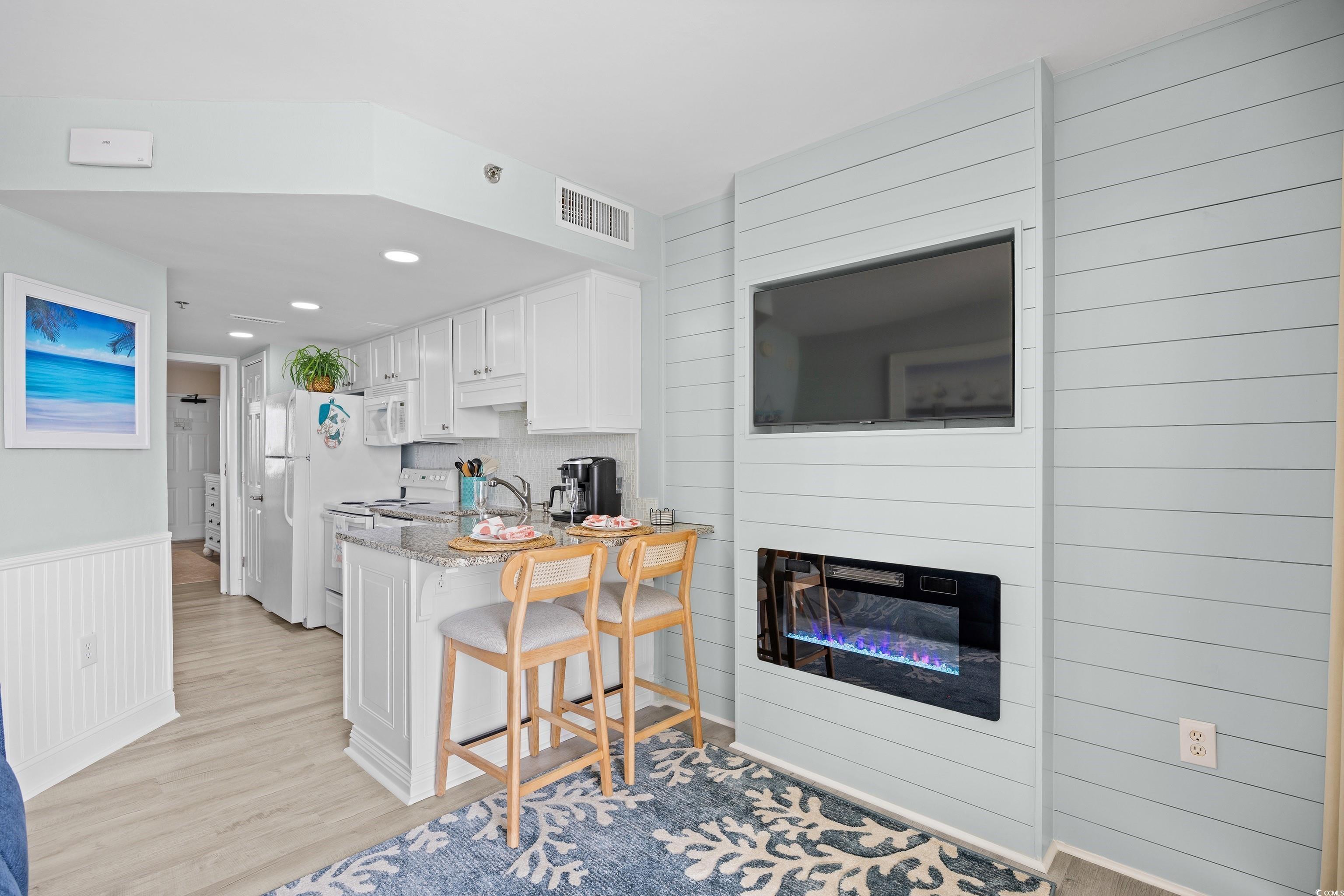 161 Seawatch Drive, Unit 1012 Myrtle Beach, SC 29572 - Photo 16 of 34 Kitchen featuring white cabinetry, a kitchen bar, light stone counters, light wood finished floors, and white appliances