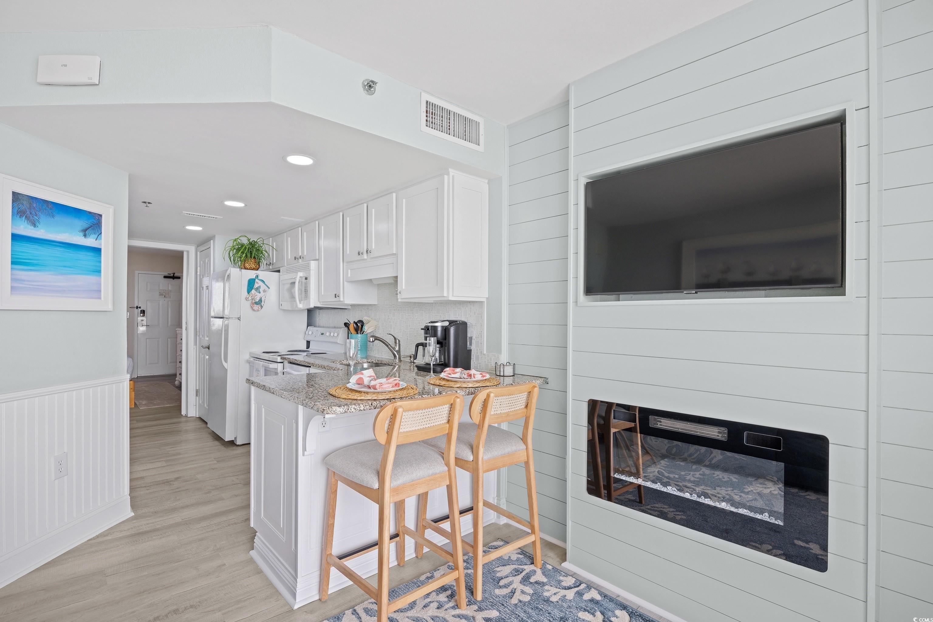 161 Seawatch Drive, Unit 1012 Myrtle Beach, SC 29572 - Photo 17 of 34 Kitchen featuring white cabinetry, a kitchen bar, white appliances, light wood-style floors, and a glass covered fireplace