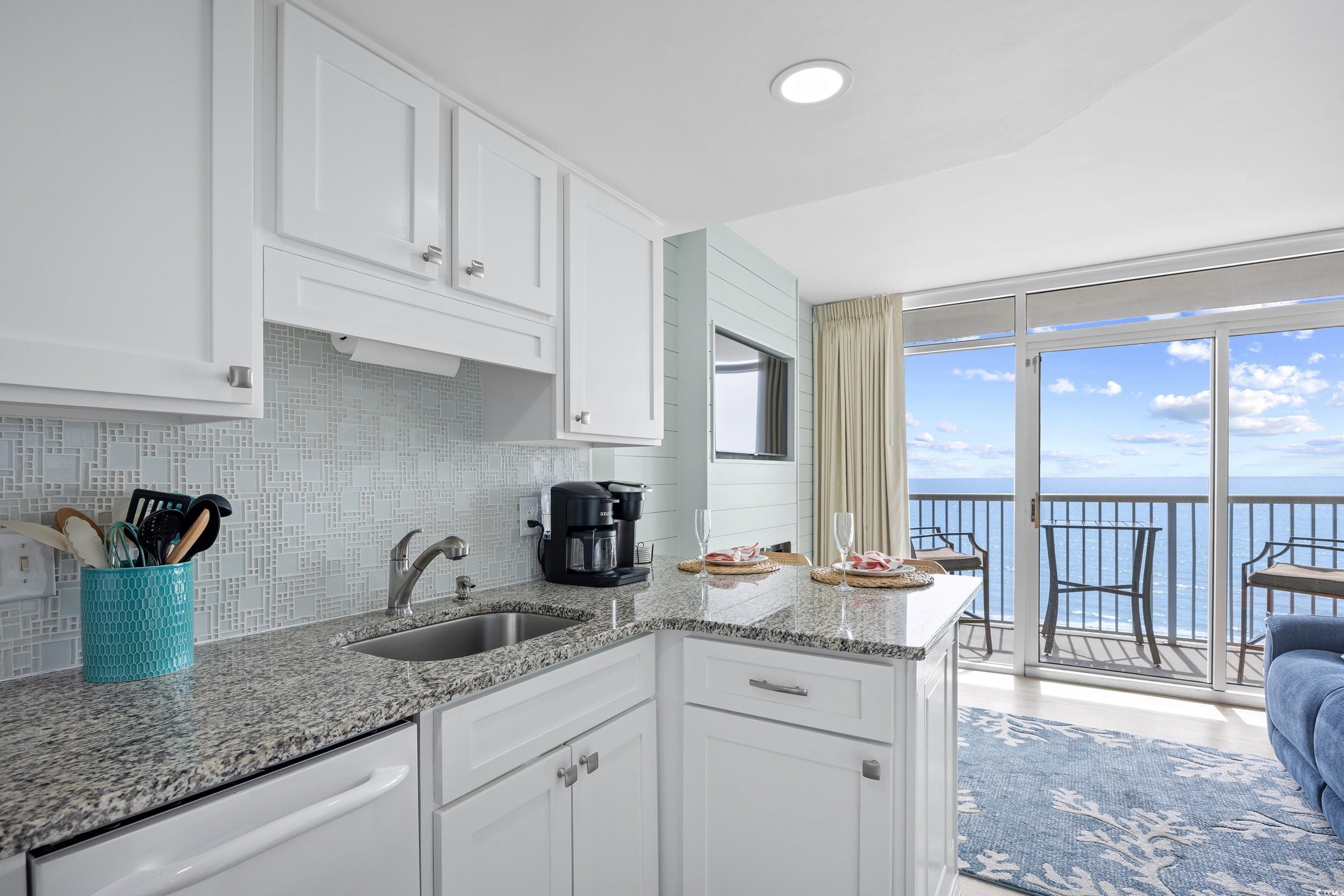 161 Seawatch Drive, Unit 1012 Myrtle Beach, SC 29572 - Photo 20 of 34 Kitchen featuring light stone counters, backsplash, a water view, white cabinetry, and floor to ceiling windows