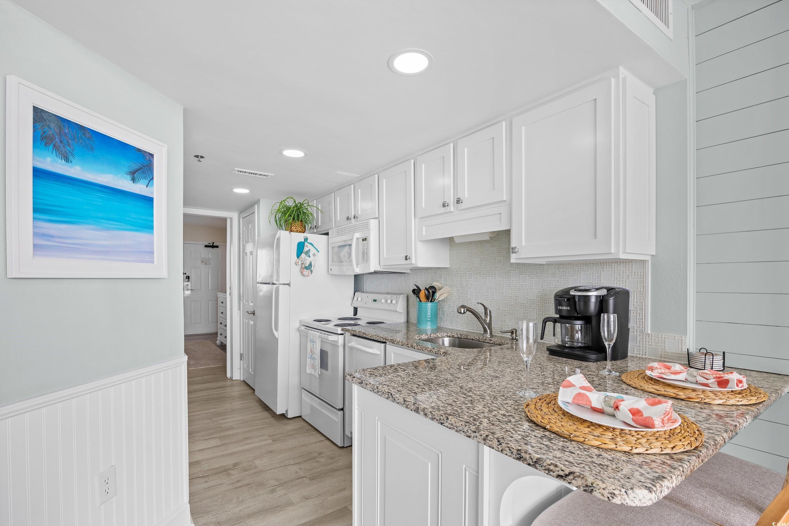 161 Seawatch Drive, Unit 1012 Myrtle Beach, SC 29572 - Photo 21 of 34 Kitchen featuring white cabinets, light stone countertops, white appliances, backsplash, and light wood-type flooring
