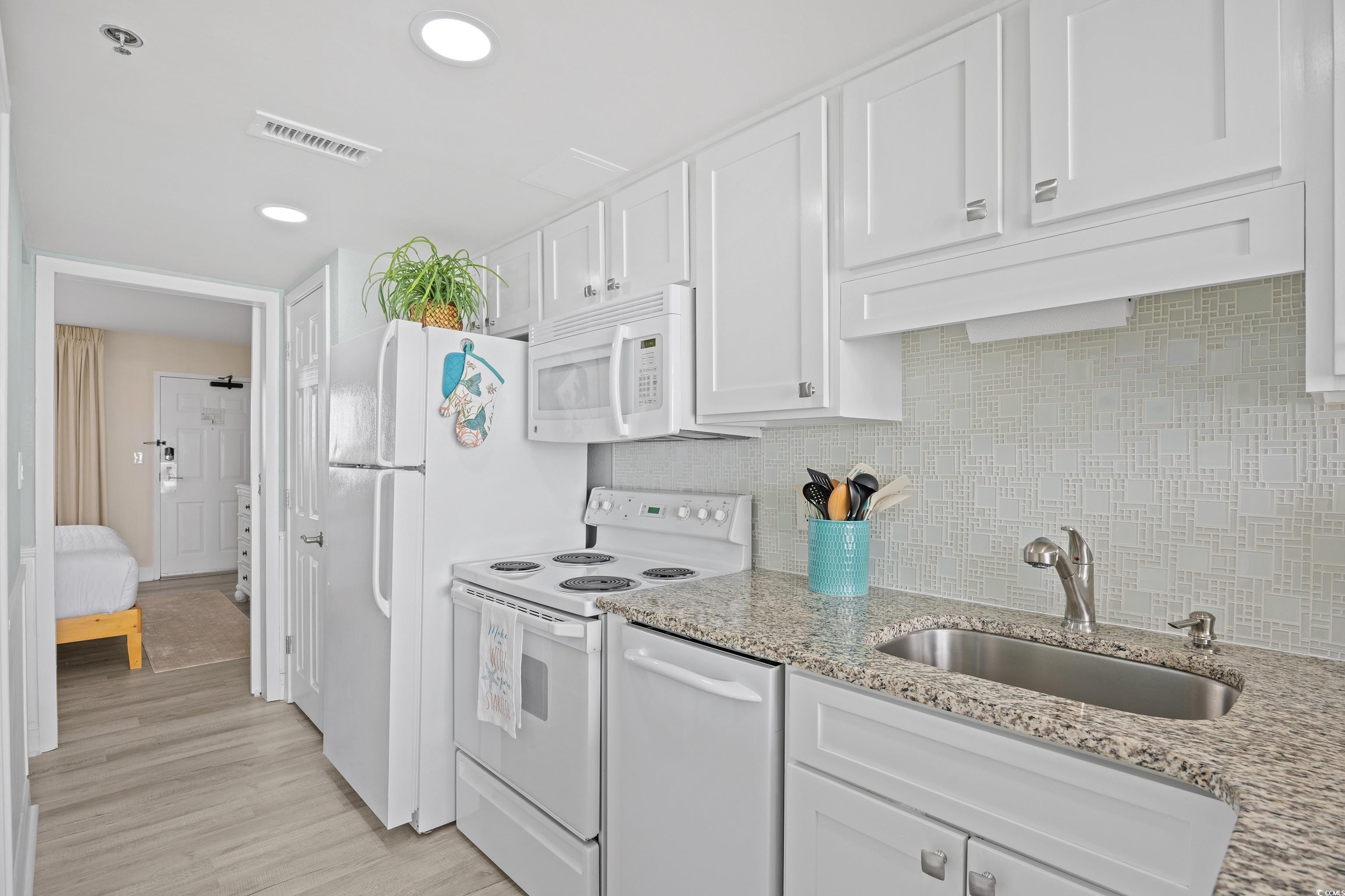 161 Seawatch Drive, Unit 1012 Myrtle Beach, SC 29572 - Photo 23 of 34 Kitchen featuring white appliances, decorative backsplash, white cabinets, light stone counters, and recessed lighting