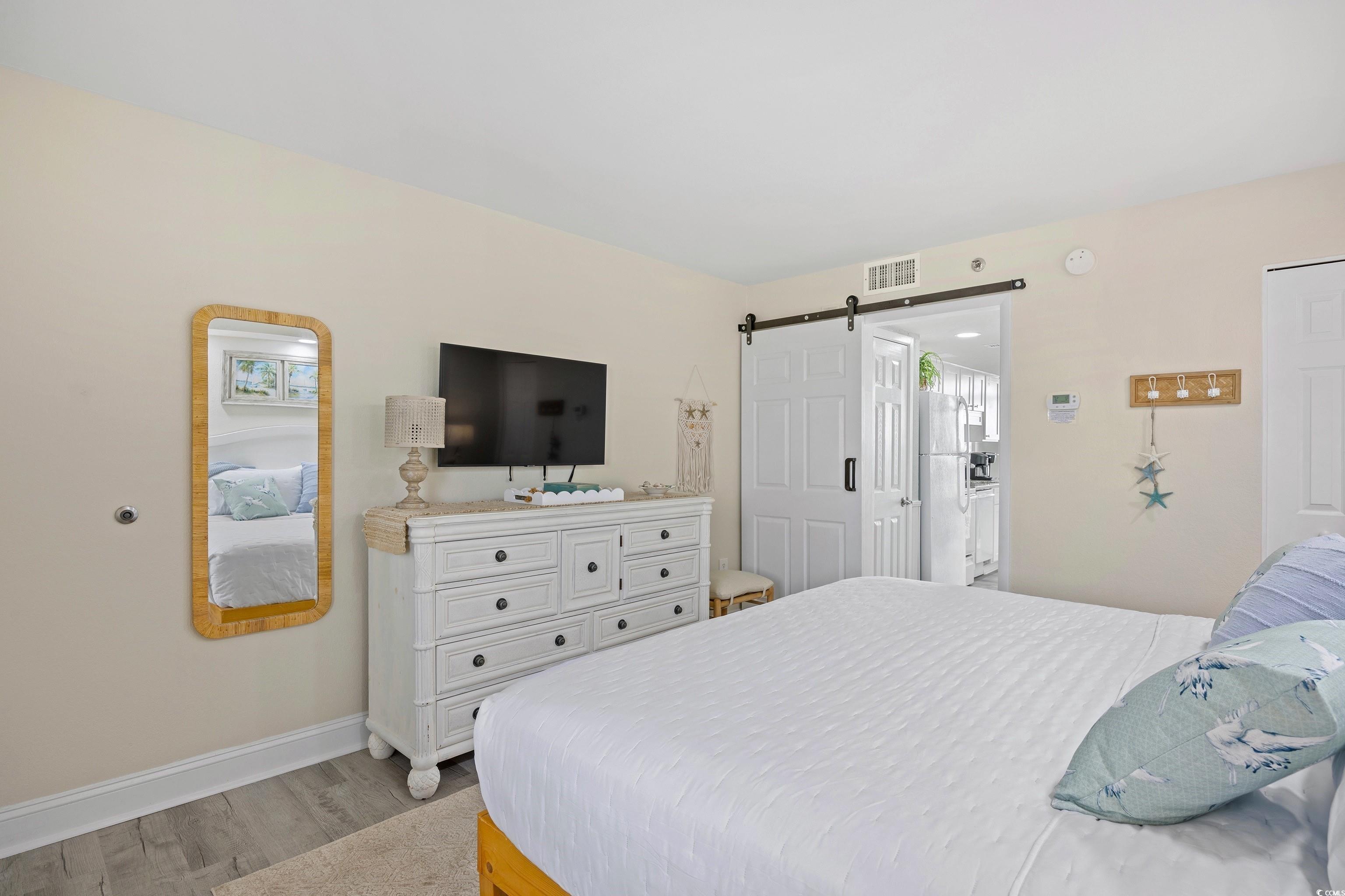 161 Seawatch Drive, Unit 1012 Myrtle Beach, SC 29572 - Photo 29 of 34 Bedroom featuring a barn door, light wood-type flooring, and freestanding refrigerator