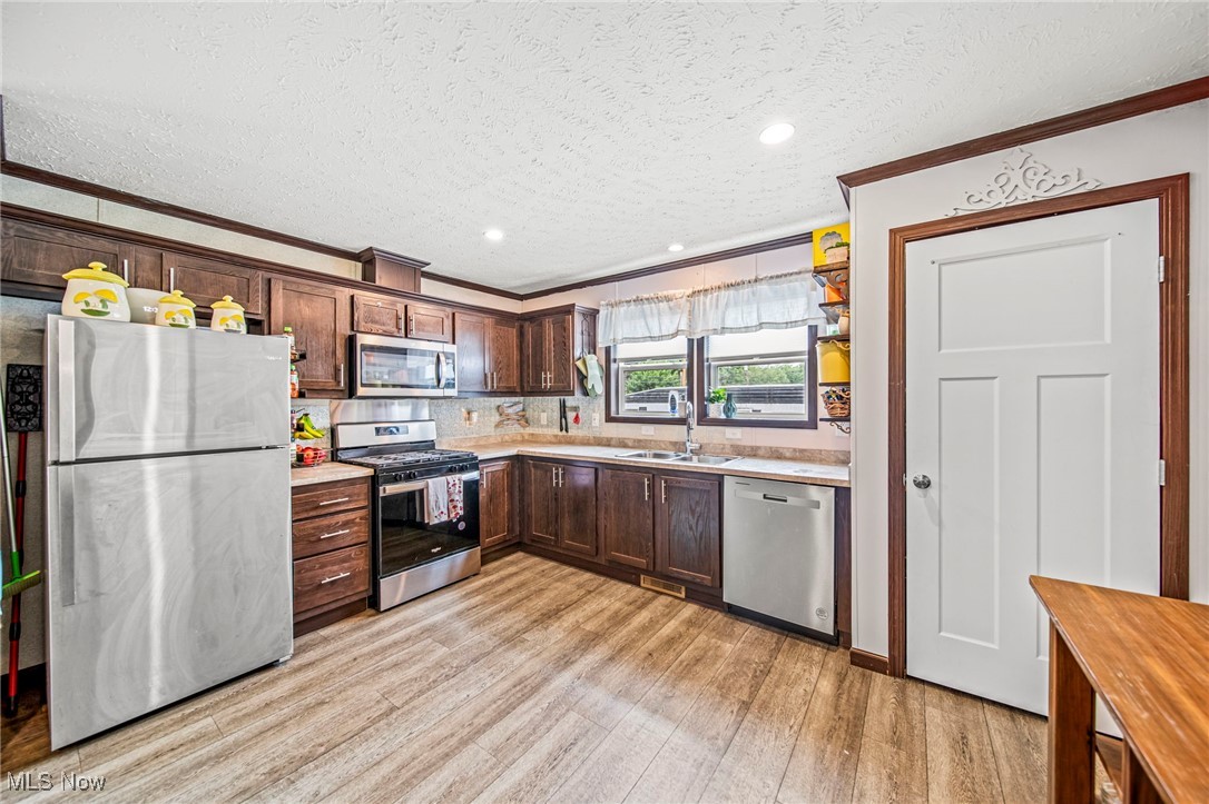 202 West Main Road, Unit LOT 13 Conneaut, OH 44030 - Photo 11 of 23 Kitchen with crown molding, appliances with stainless steel finishes, a textured ceiling, light wood-type flooring, and dark brown cabinets