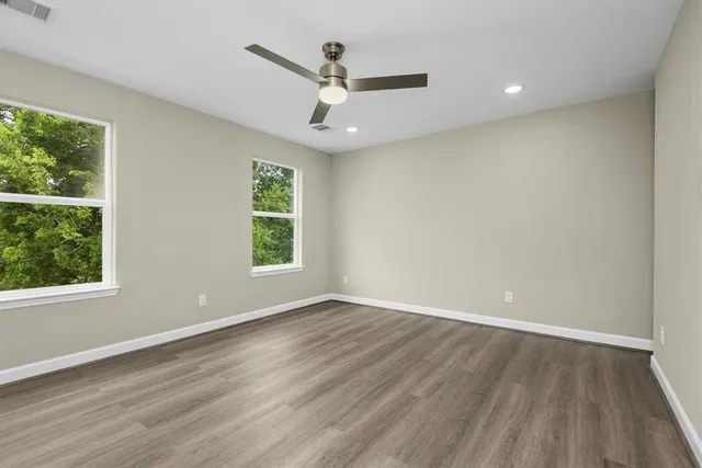 an empty room with wooden floor ceiling fan and windows