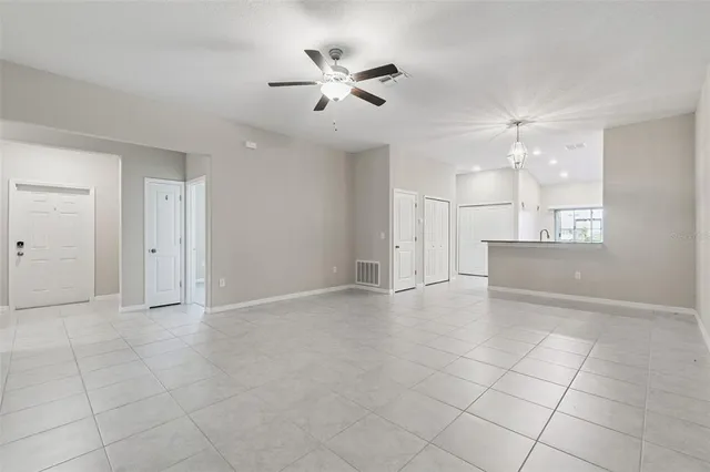 an empty room with chandelier fan and windows