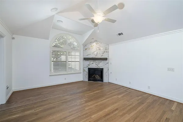 an empty room with wooden floor chandelier fan and windows