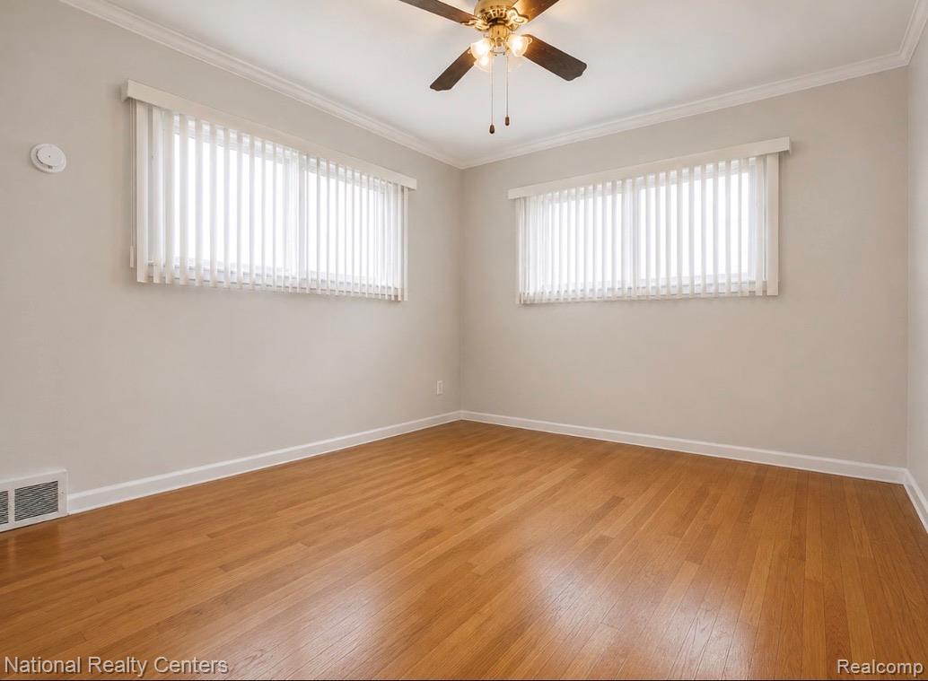 7285 Helen Street Center Line, MI 48015 - Photo 13 of 32 Light-filled room featuring wood-finish flooring, two windows with vertical blinds, a ceiling fan with light fixture, white crown molding, and white baseboards