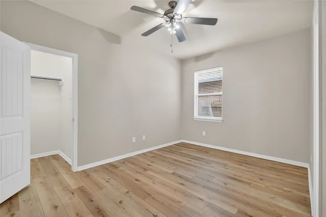 a view of an empty room with wooden floor and a ceiling fan