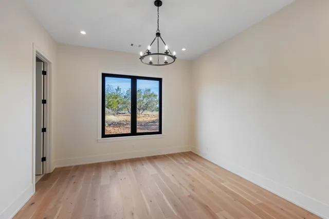 an empty room with wooden floor chandelier and windows
