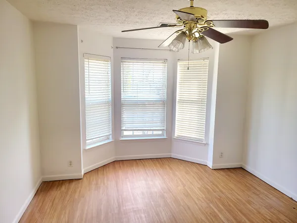 an empty room with wooden floor fan and windows