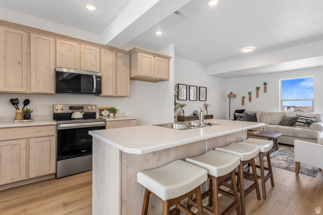 636 West Caroles Way, Unit 7 Tooele, UT 84074 - Photo 11 of 31 Open-concept kitchen featuring light-toned wood cabinetry, stainless steel appliances, and a central island with integrated seating